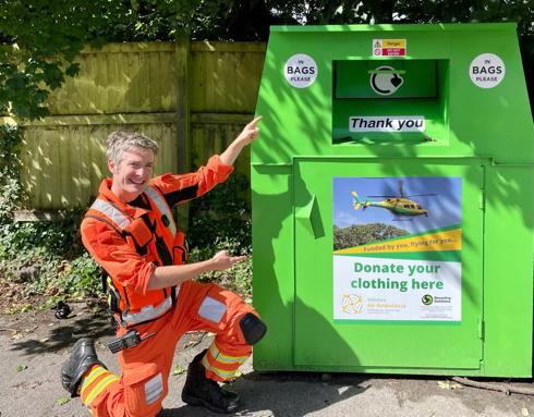 A doctor wearing an orange flight suit, crouched and pointing at a WAA green clothing bank