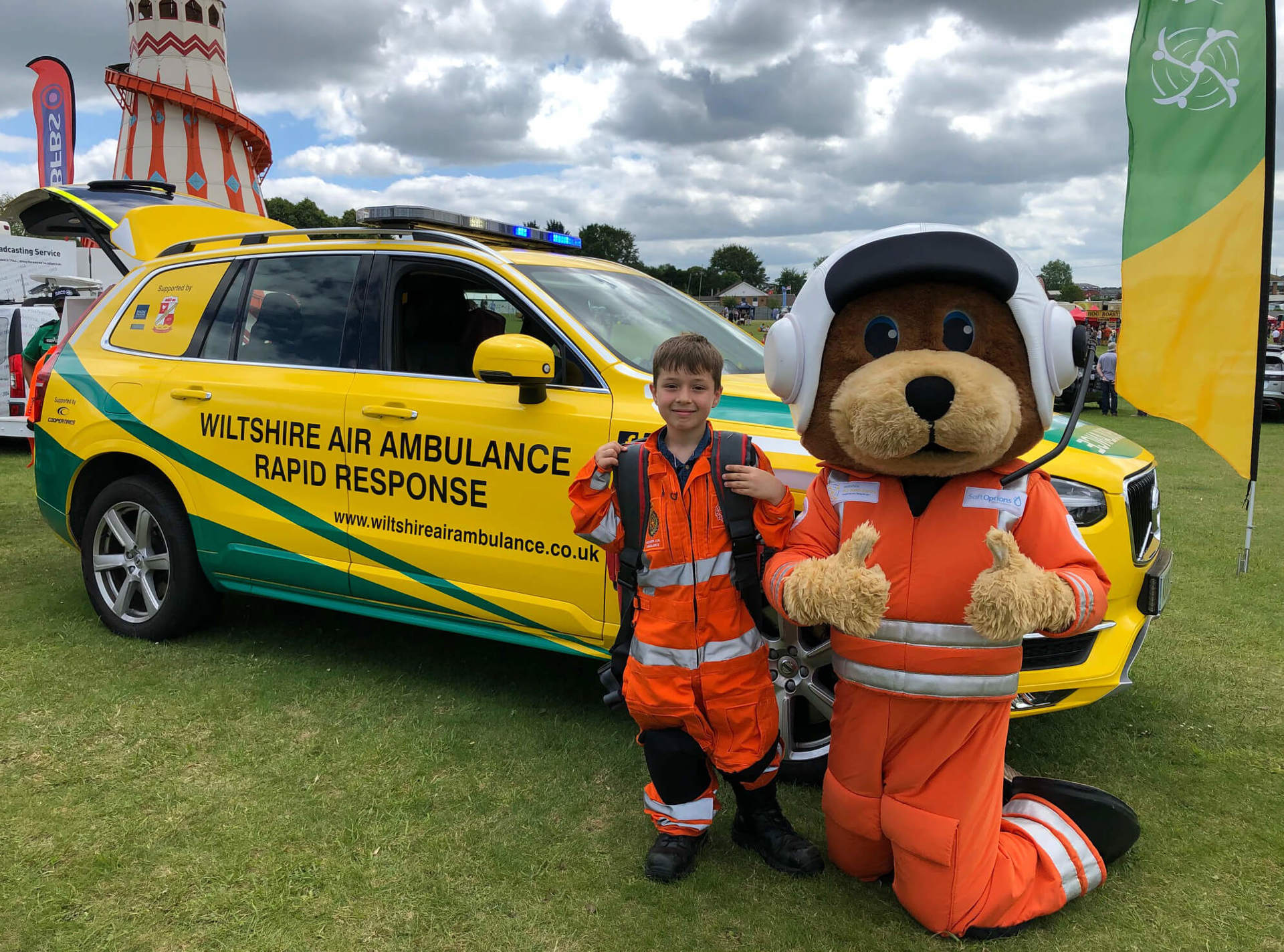 Mascot Wilber wearing an orange flight suit next to a child wearing a small orange flight suit in front of the critical care car.