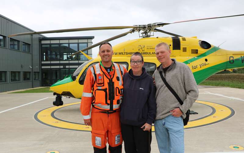 A former patient and their partner stood with a critical care paramedic in front of the Bell-429 helicopter.