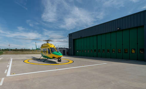 The yellow and green helicopter landed on the helipad against a blue sky with the rotor blades turning.