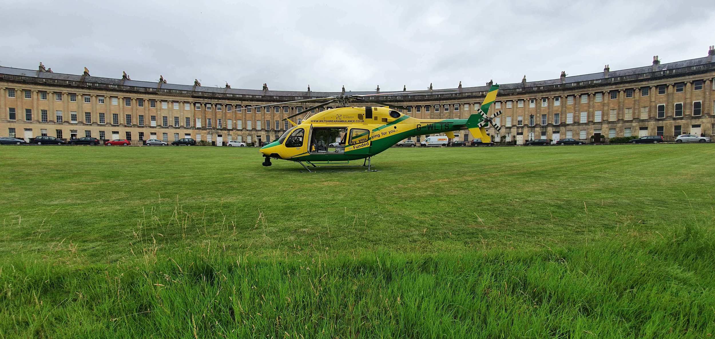 Wiltshire Air Ambulance's yellow and green helicopter parked in front of the Royal Crescent in Bath