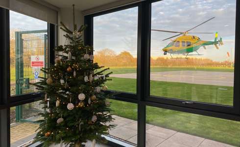 A Christmas tree decorated in gold baubles located in the airbase reception with the helicopter landing in the background.
