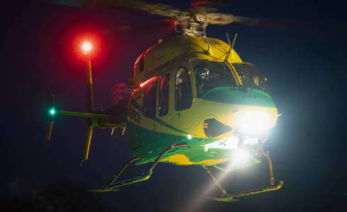 The Bell-429 helicopter in flight at night with a bright white light at the front and a bright red light on the tail of the helicopter.