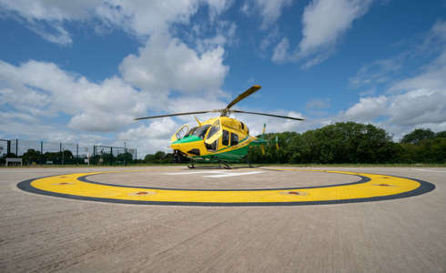 The yellow and green helicopter landed on the helipad against a blue sky with its front two doors open.