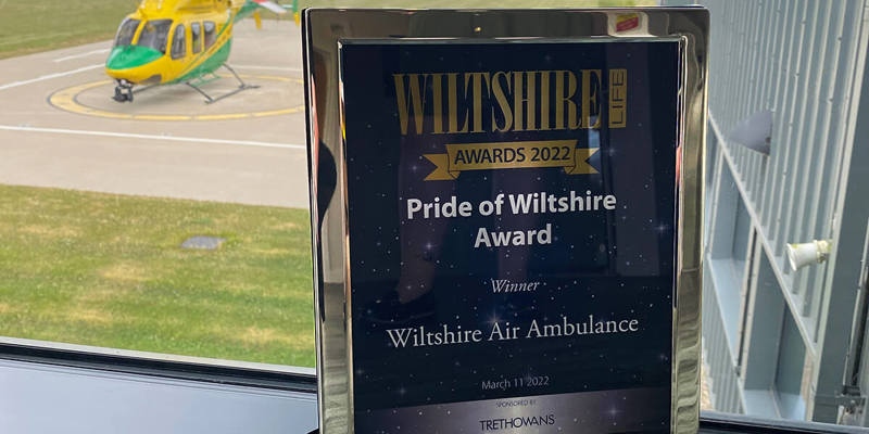A silver framed 'Pride of Wiltshire' award on a window ledge with the WAA helicopter in the background