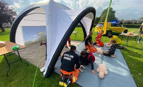 Three paramedics delivering Emergency Awareness Training in a blow up gazebo with members of the public using mannequins.