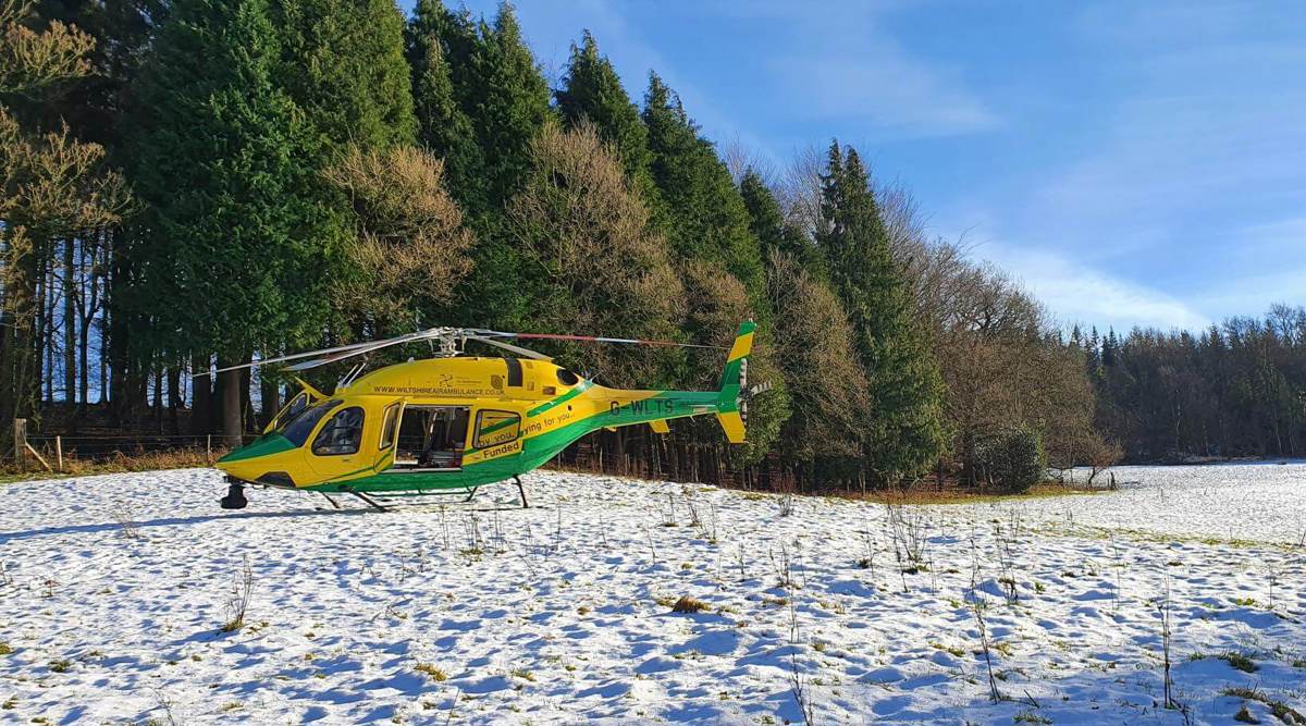 A photograph of the yellow and green helicopter landed in a snowy field with trees in the background.