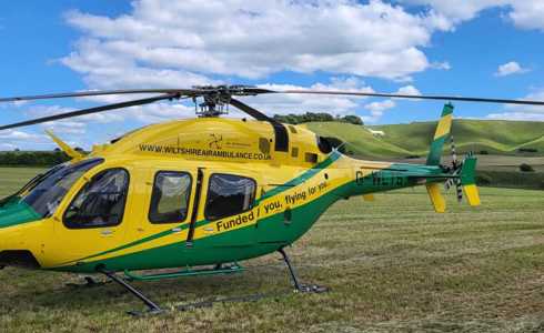 Yellow and green Wiltshire Air Ambulance helicopter landed in a field with white horse in the background