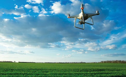A drone flying in the blue skies over a green field
