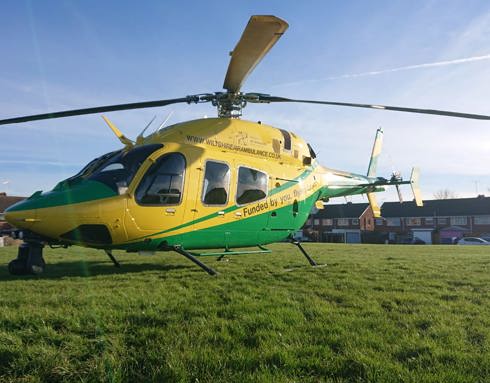 A yellow and green helicopter landed on a green in Swindon, with houses behind