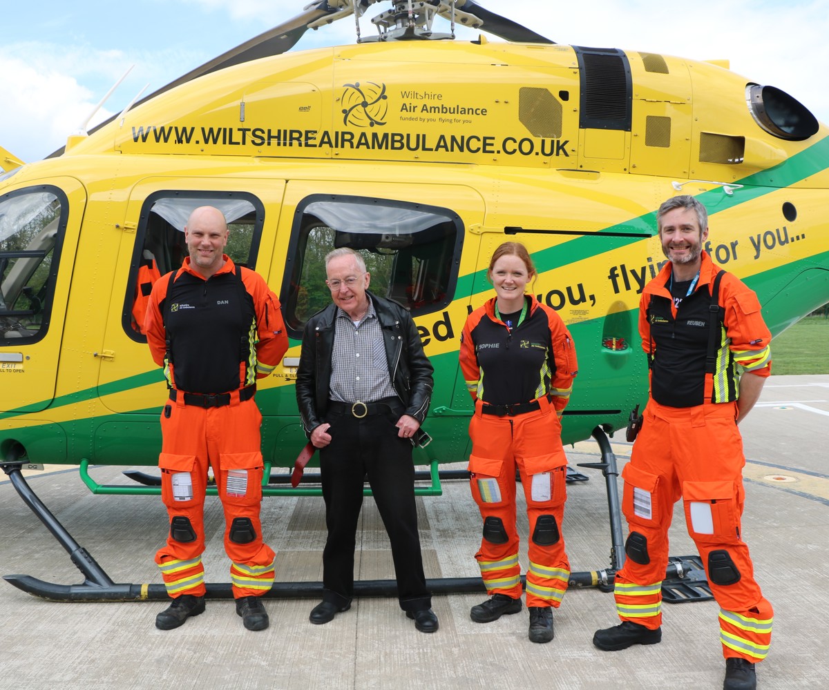 Patient Martyn Dormer standing in front of the helicopter with critical care paramedics Dan and Sophie, and doctor Reuben who are wearing orange flight suits,