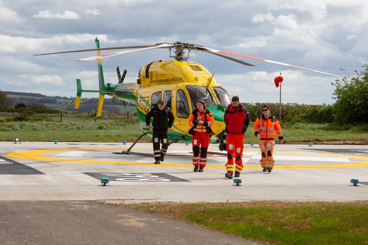 Yellow and green helicopter landed at Salisbury District Hospital helipad launch with crew walking towards camera