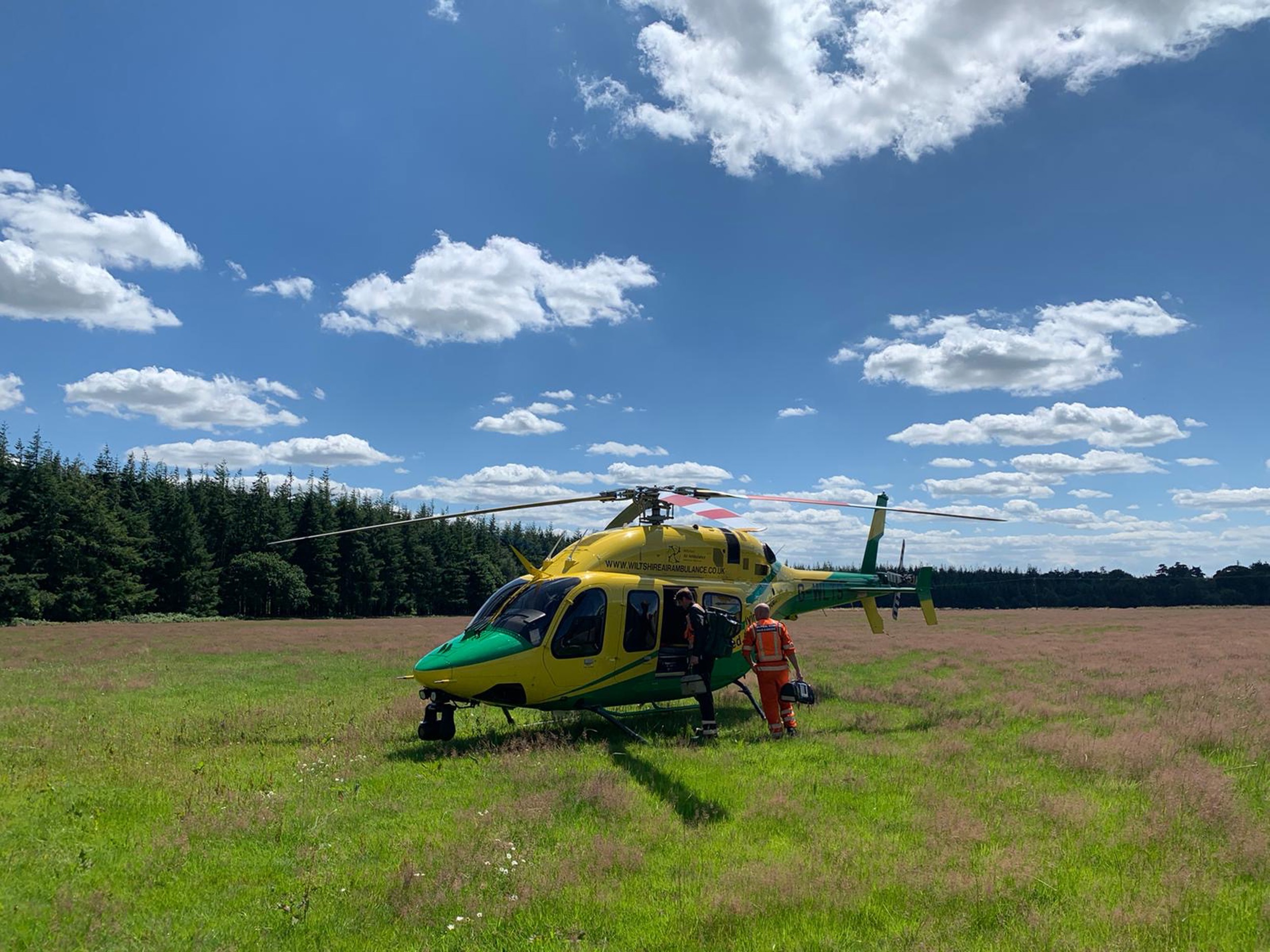 A photo of a yellow and green helicopter landed in a field with blue sky
