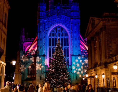 The exterior of Bath Abbey lit up with Christmas lights and a Christmas tree