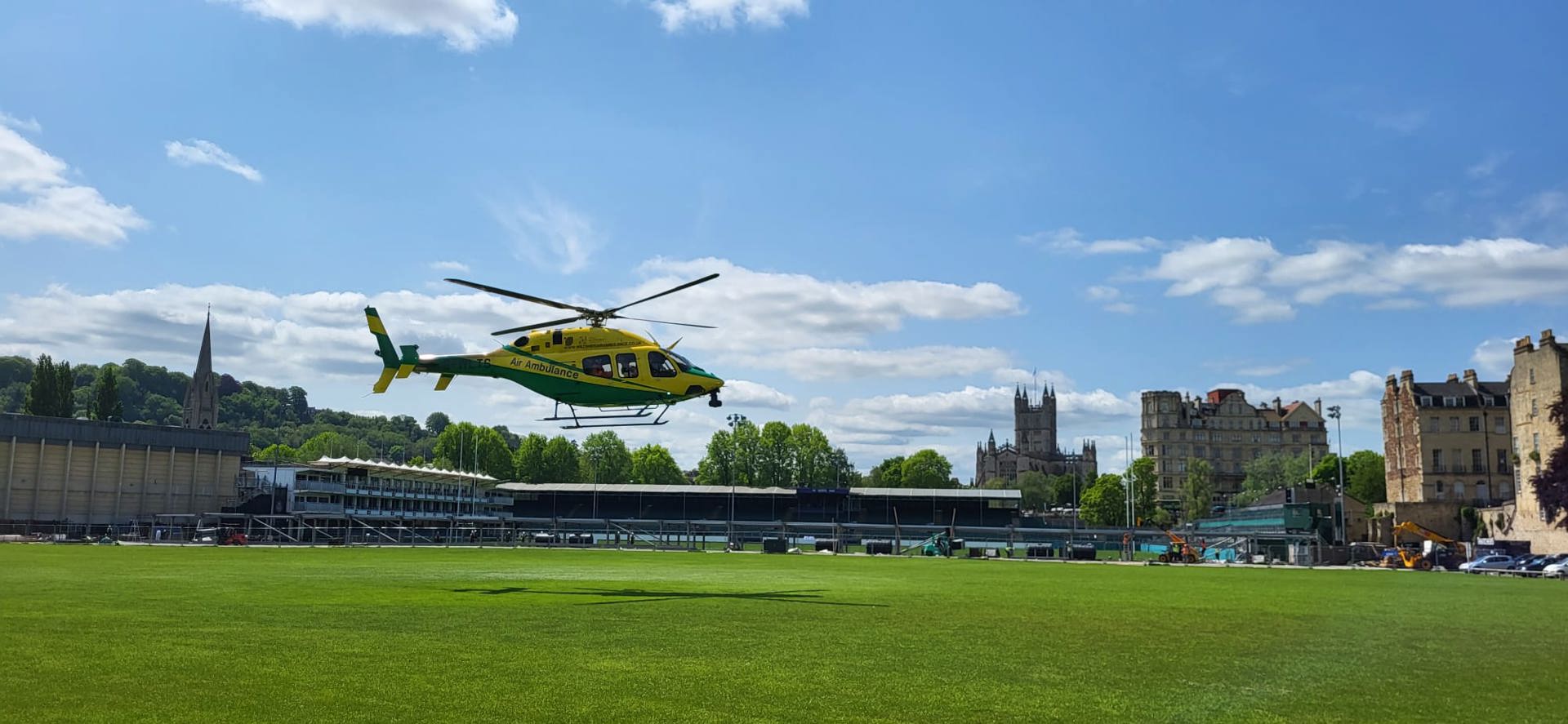 Wiltshire Air Ambulance's yellow and green helicopter landing at the Recreation Ground in Bath