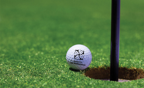 A Wiltshire Air Ambulance branded golf ball on the edge of a golf hole