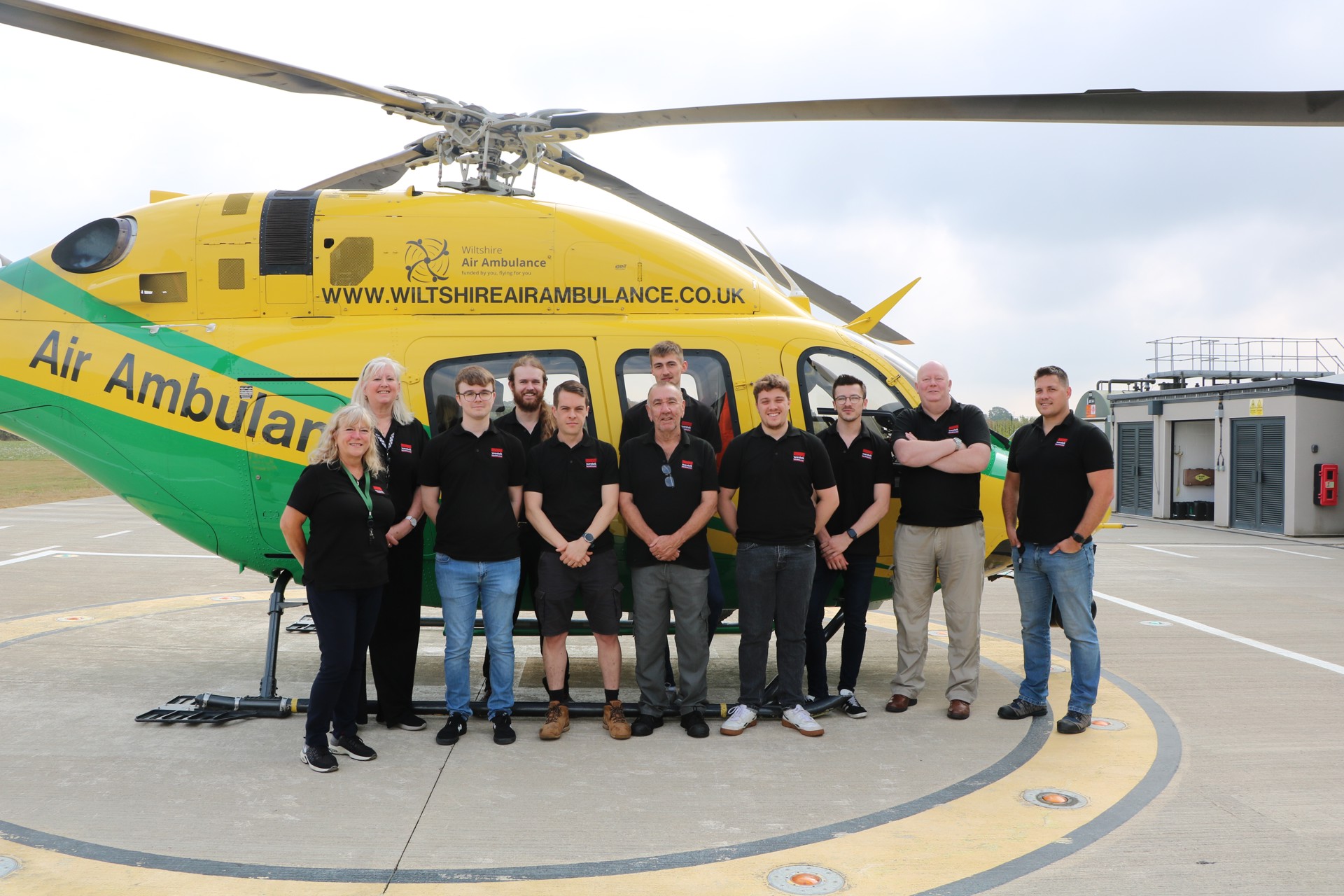 A group from Westek having their photo taken with a yellow and green helicopter