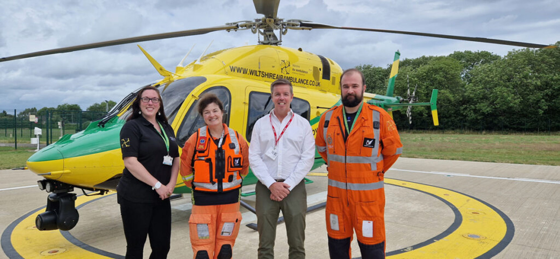 A member from Goodman Nash in front of wiltshire air ambulance's helicopter, with two paramedics and a charity team member