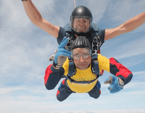 A volunteer taking part in a charity skydive. They are wearing goggles and a yellow t-shirt.