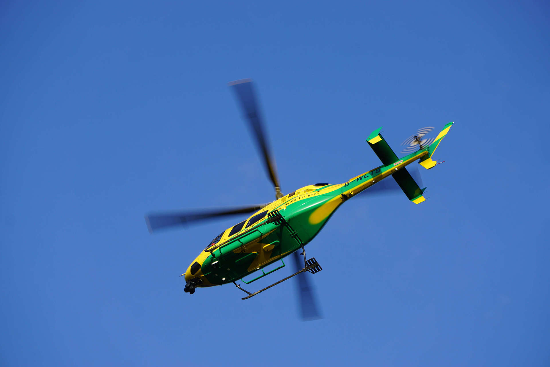 The yellow and green helicopter in flight against a blue sky.