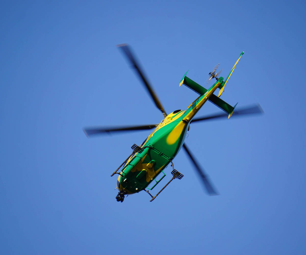 The yellow and green helicopter in flight against a blue sky.