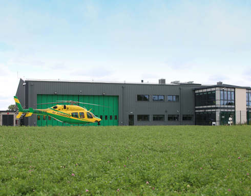 A panoramic view of the Wiltshire Air Ambulance helipad and airbase featuring the yellow and green Bell-429 helicopter on its helipad.