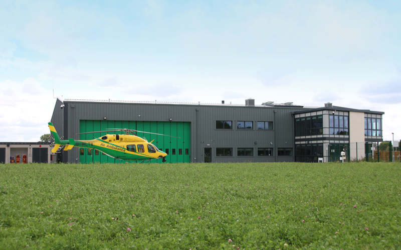 A panoramic view of the Wiltshire Air Ambulance helipad and airbase featuring the yellow and green Bell-429 helicopter on its helipad.