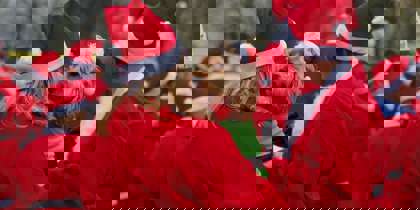 A group of people wearing red Santa suits, with one holding a dog dressed as an elf