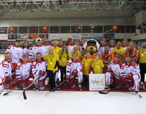 A large group photo on the ice rink at the Swindon Link Centre of Wiltshire Air Ambulance staff, volunteers and crew alongside ice hockey platers and the WAA teddy bear mascot, Wilber.