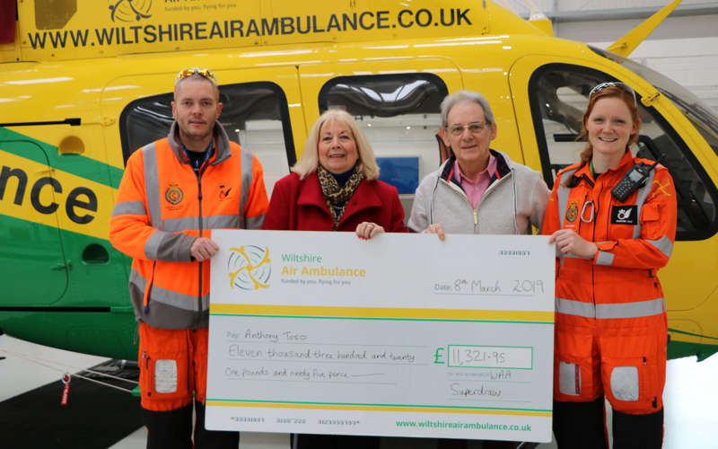 A group photo of a Superdraw winner and their partner with two paramedics. The group are stood in front of the helicopter in the hangar.