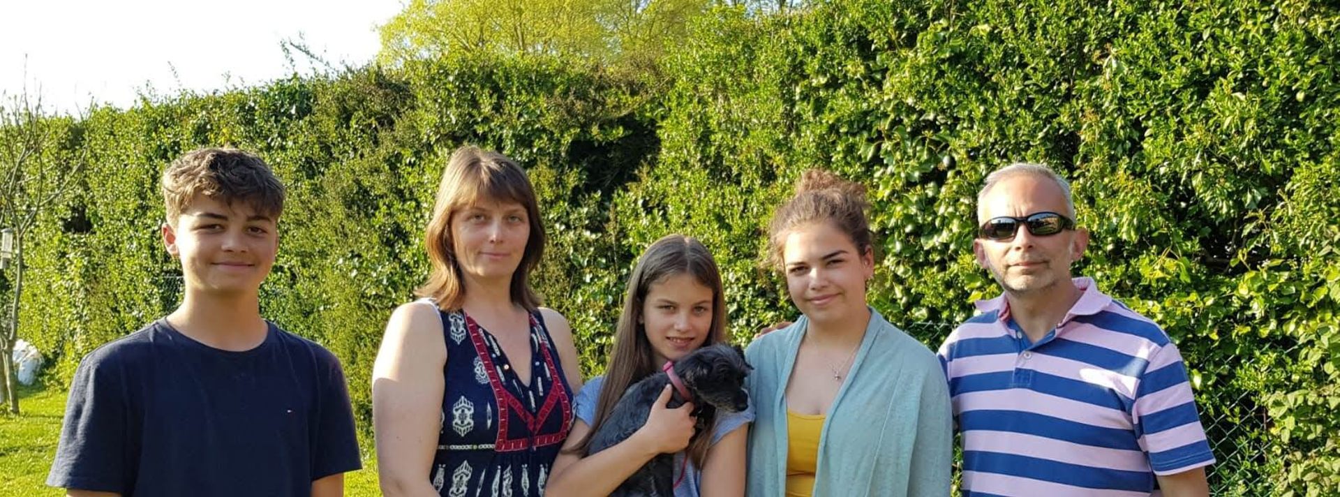 A family and their dog stood in a garden against a green hedge