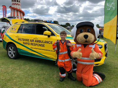 Mascot Wilber wearing an orange flight suit next to a child wearing a small orange flight suit in front of the critical care car.