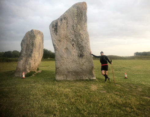 A supporter wearing black sports gear who is stood next to the Avebury Stones after taking part in the Race to the Stones event.