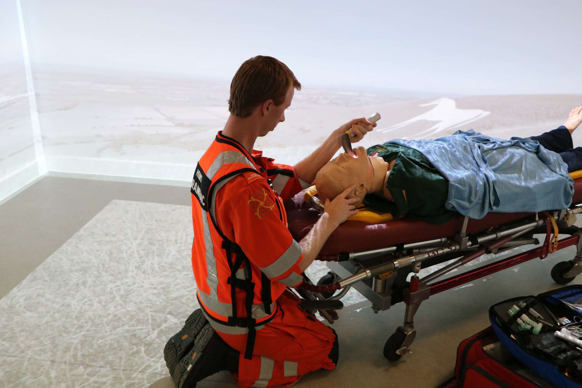 A critical care paramedic doing training in a simulation room using medical equipment and a mannequin.