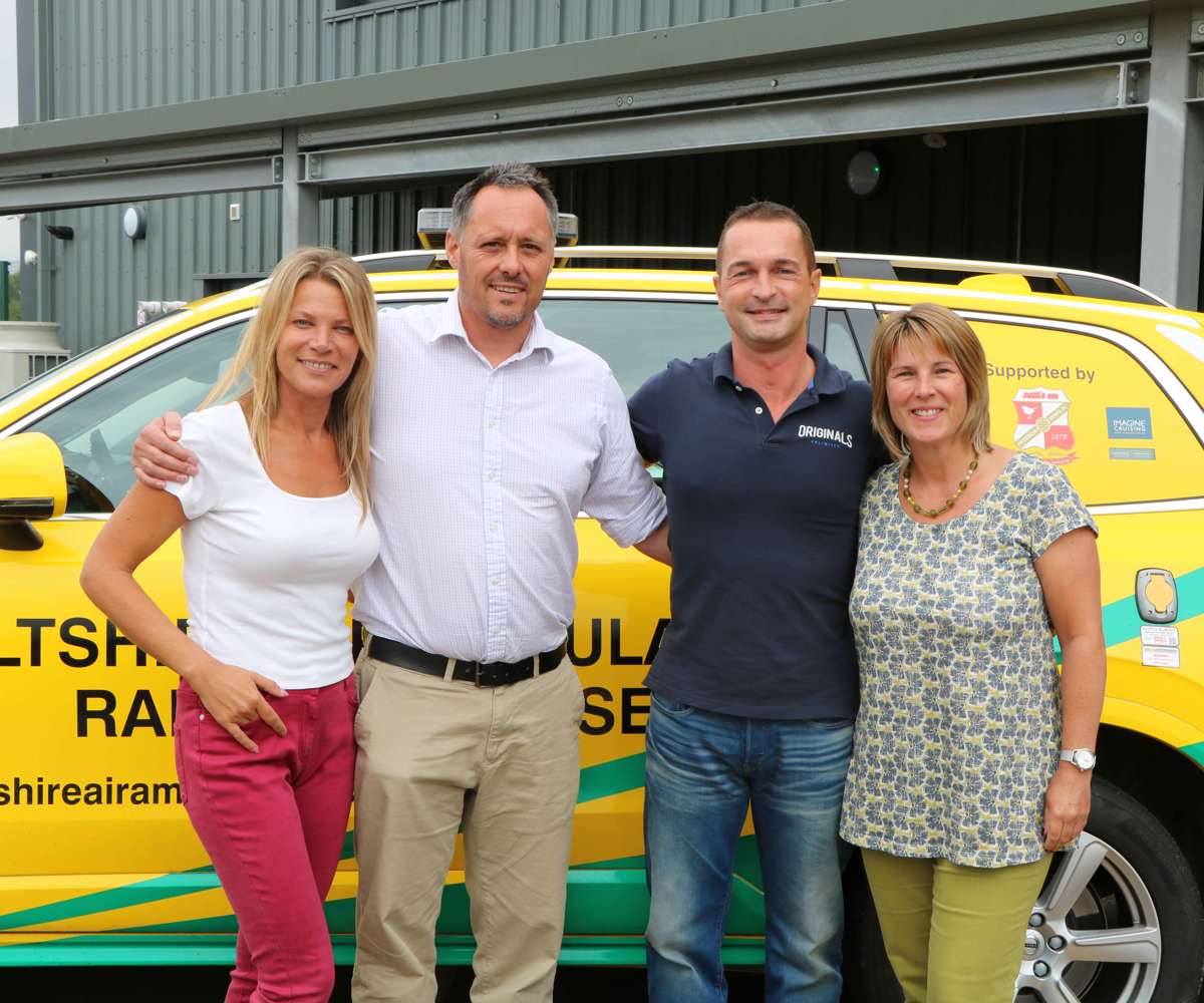 A former patient and their partner visiting Wiltshire Air Ambulance, the group are with a paramedic and pilot stood in front of the critical care car.