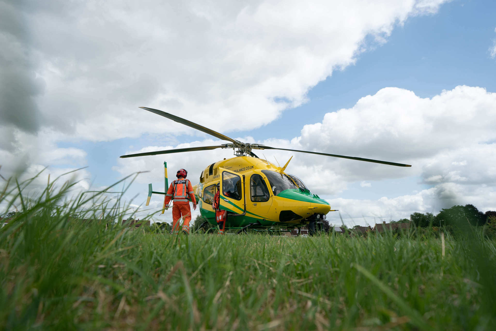 A photo of the yellow and green Bell-429 helicopter in a grassy field featuring two critical care paramedics.