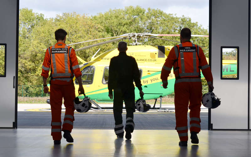 Two paramedics and a pilot walking towards the helicopter from inside the hangar.