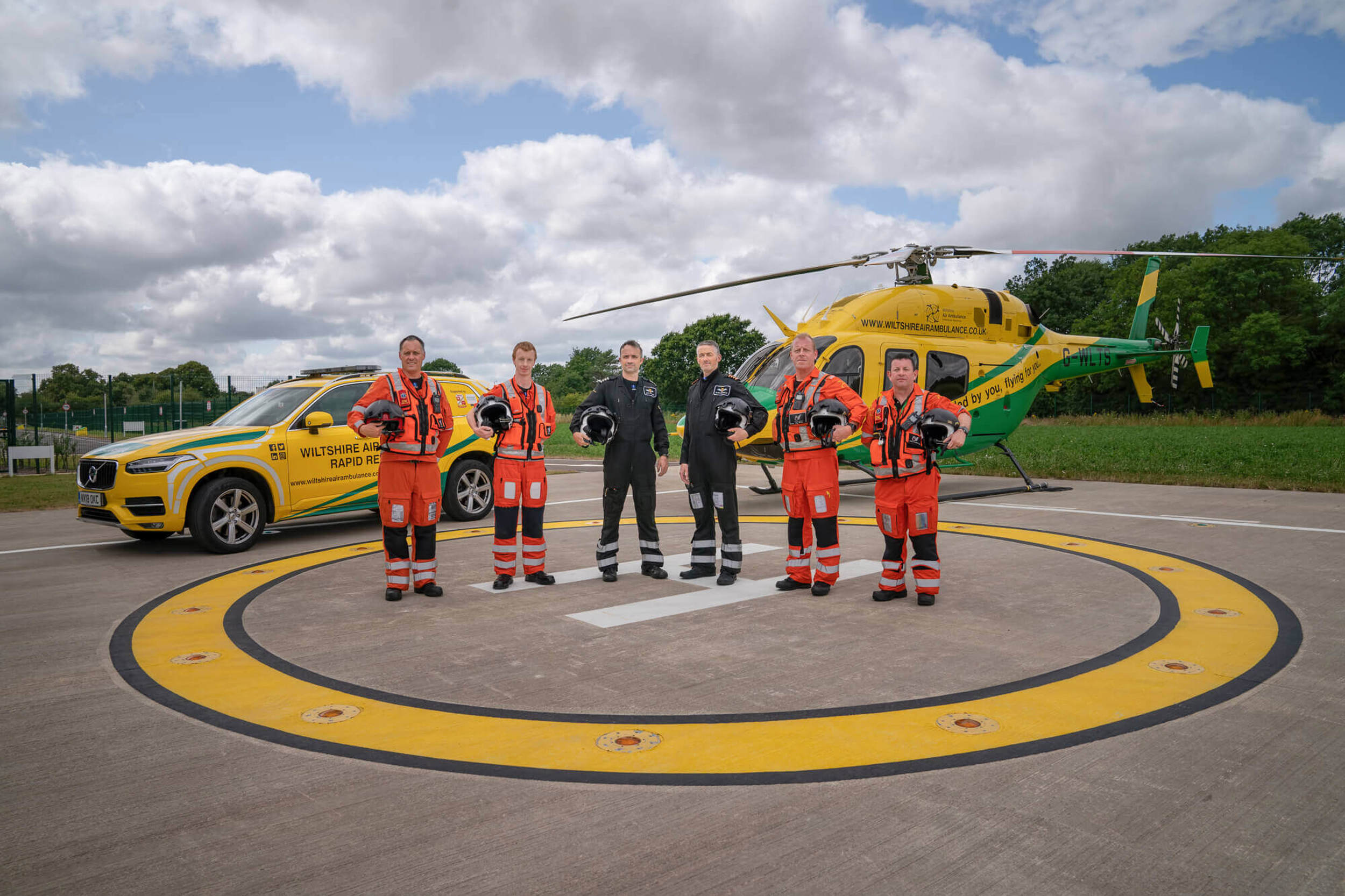A group photo of four paramedics and two pilots stood on the helipad in front of the helicopter and critical care cars.