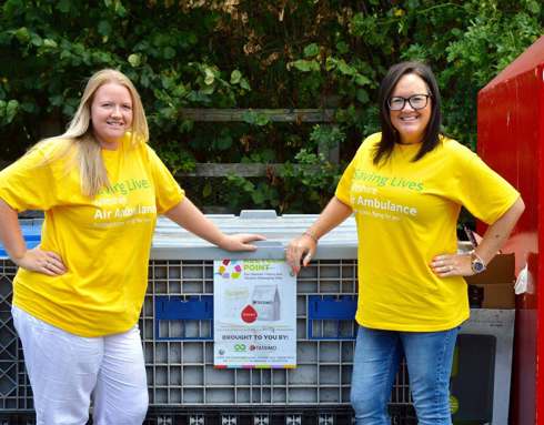 A photo of two volunteers wearing yellow t-shirts in front of a Terracycle recycling point.