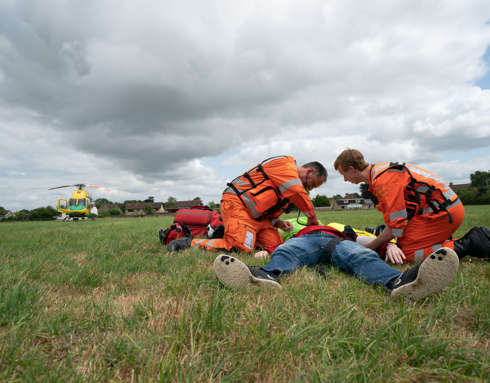 A staged incident in a field with two paramedics and a patient with the helicopter in the background.