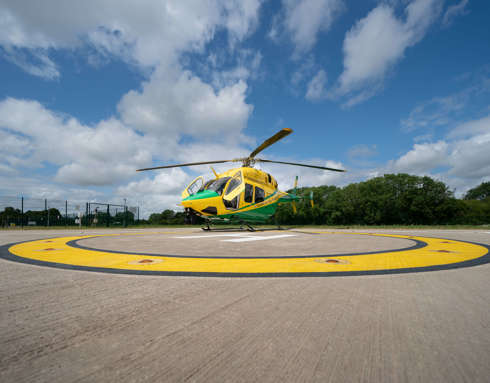 The Wiltshire Air Ambulance green and yellow branded Bell-429 sat on the helipad at the airbase on a sunny day.