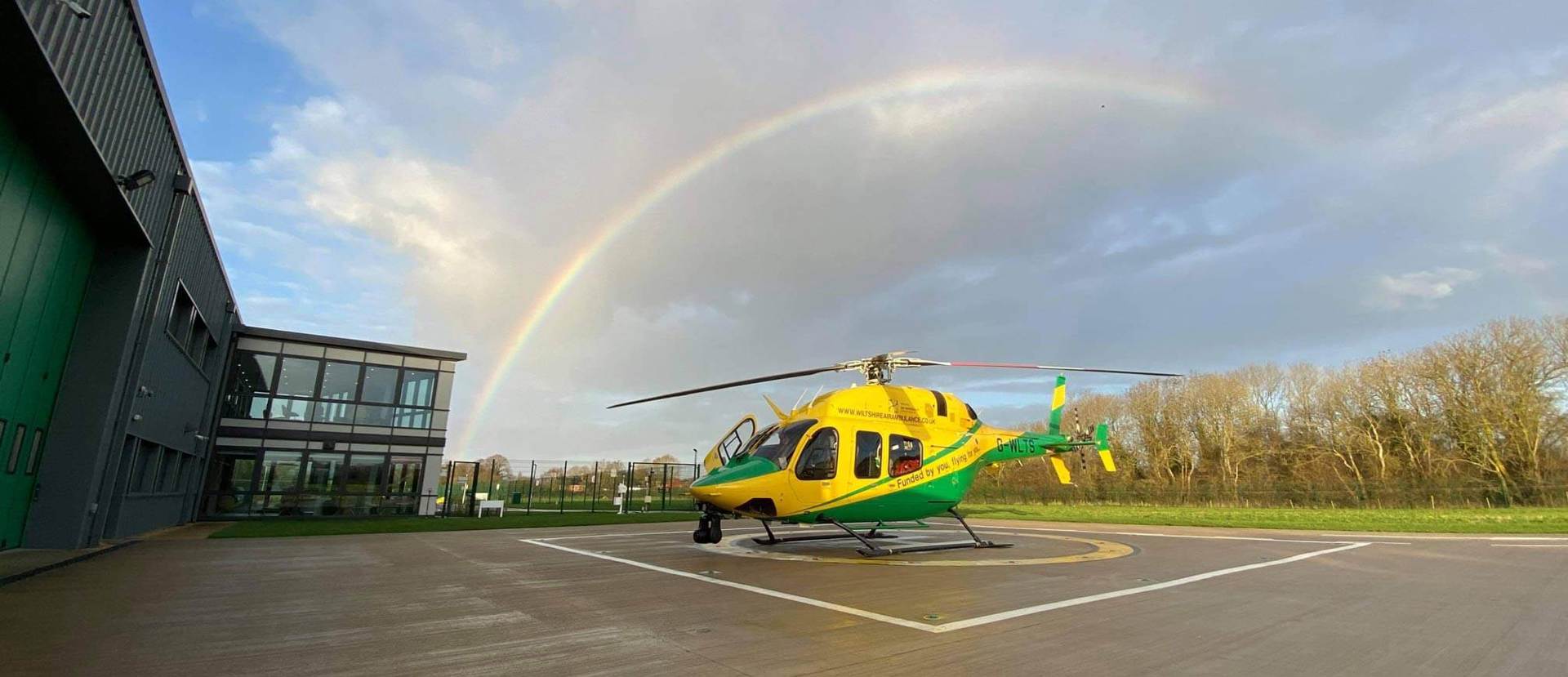 The Bell-429 helicopter on the helipad with a rainbow in the sky behind 