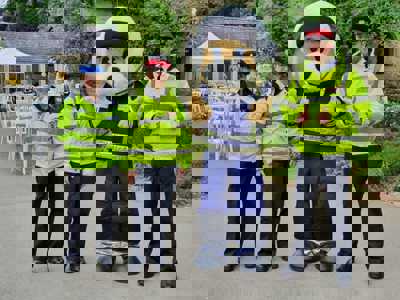 Marsha the teddy bear pilot mascot stood in a courtyard with three police officers wearing high-vis jackets.