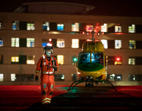 A critical care paramedic stood in front of the helicopter which has landed on the helipad at Great Western Hospital at night.