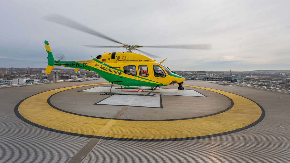 The yellow and green helicopter landed with its rotor blades turning on a hospital helipad on a grey day.