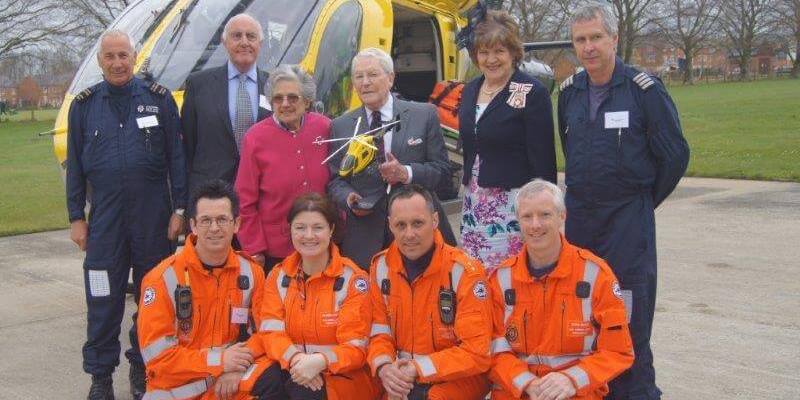 A group photo of four paramedics and two pilots suits stood in front of the MD-902 helicopter in Devizes with Dr Dick Risley Pritchard, who has been presented with a model helicopter.