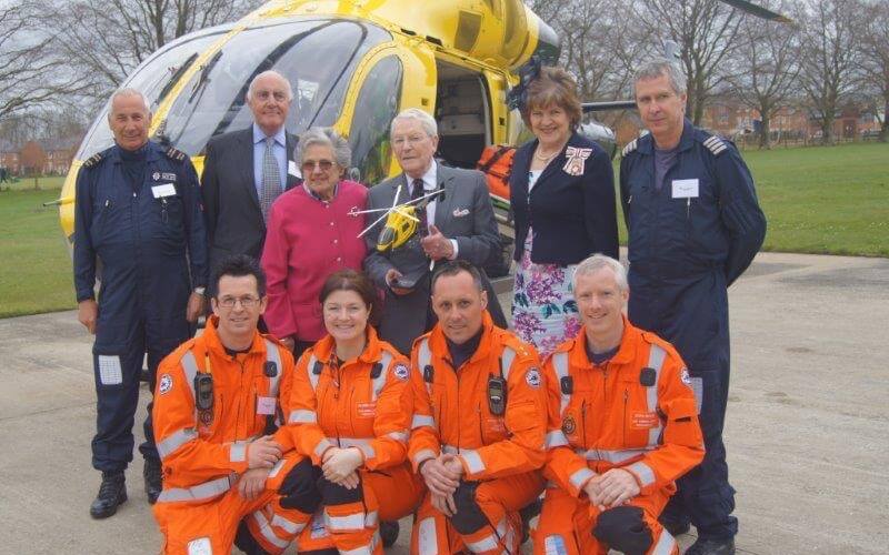 A group photo of four paramedics and two pilots suits stood in front of the MD-902 helicopter in Devizes with Dr Dick Risley Pritchard, who has been presented with a model helicopter.