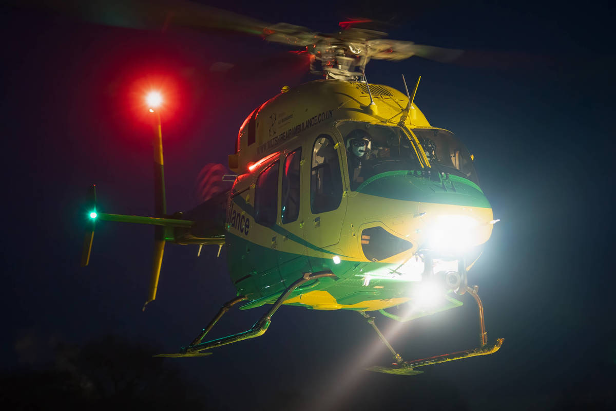 The Bell-429 helicopter in flight at night with a bright white light at the front and a bright red light on the tail of the helicopter.