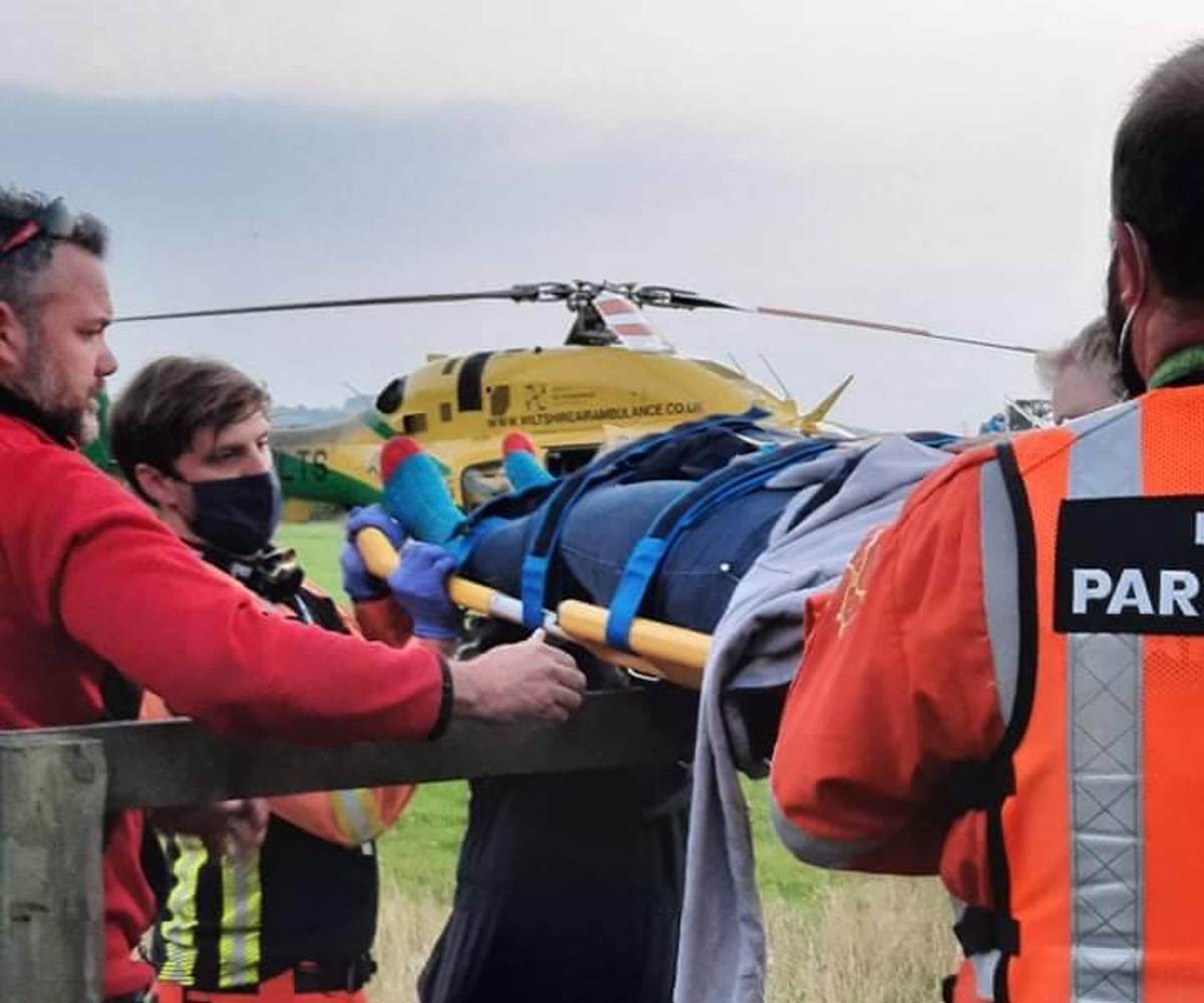 A patient being carried over a fence on a stretcher. The Bell 429 helicopter is in the background.