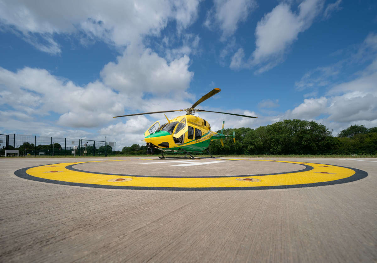 The yellow and green helicopter landed on the helipad against a blue sky with its front two doors open.